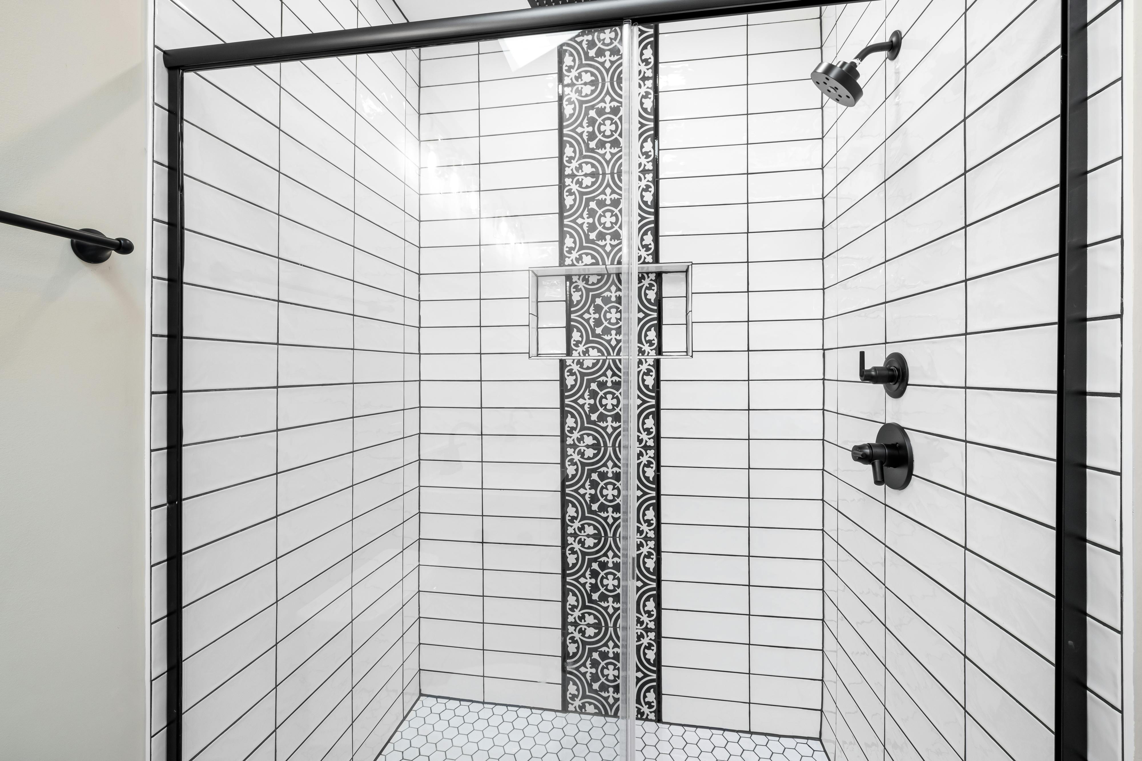 Stylish shower with white subway tiles and a striking black patterned accent wall for a modern touch.